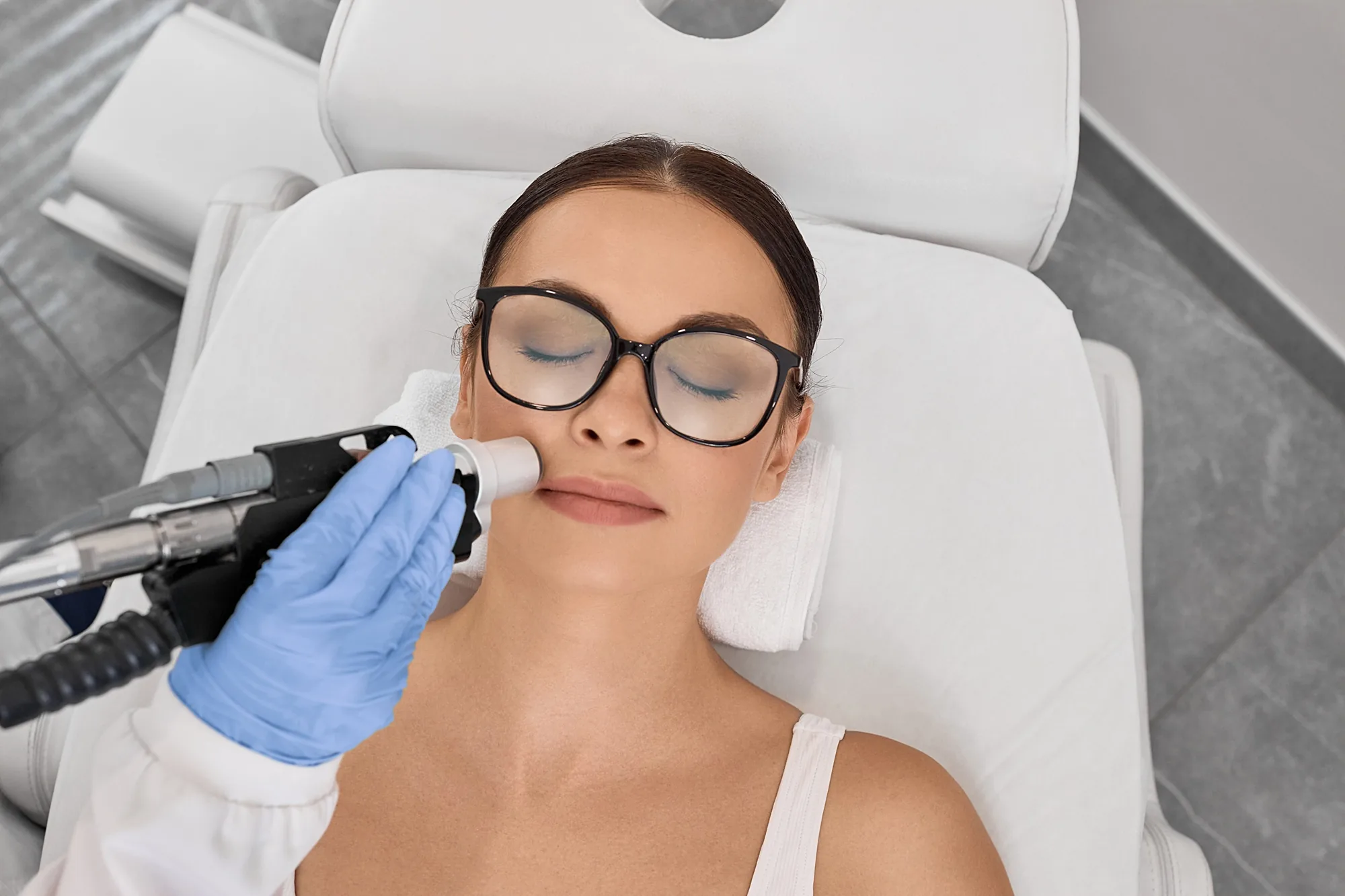 Overhead view of a woman in protective eyewear receiving a laser facial skin treatment at a clinic